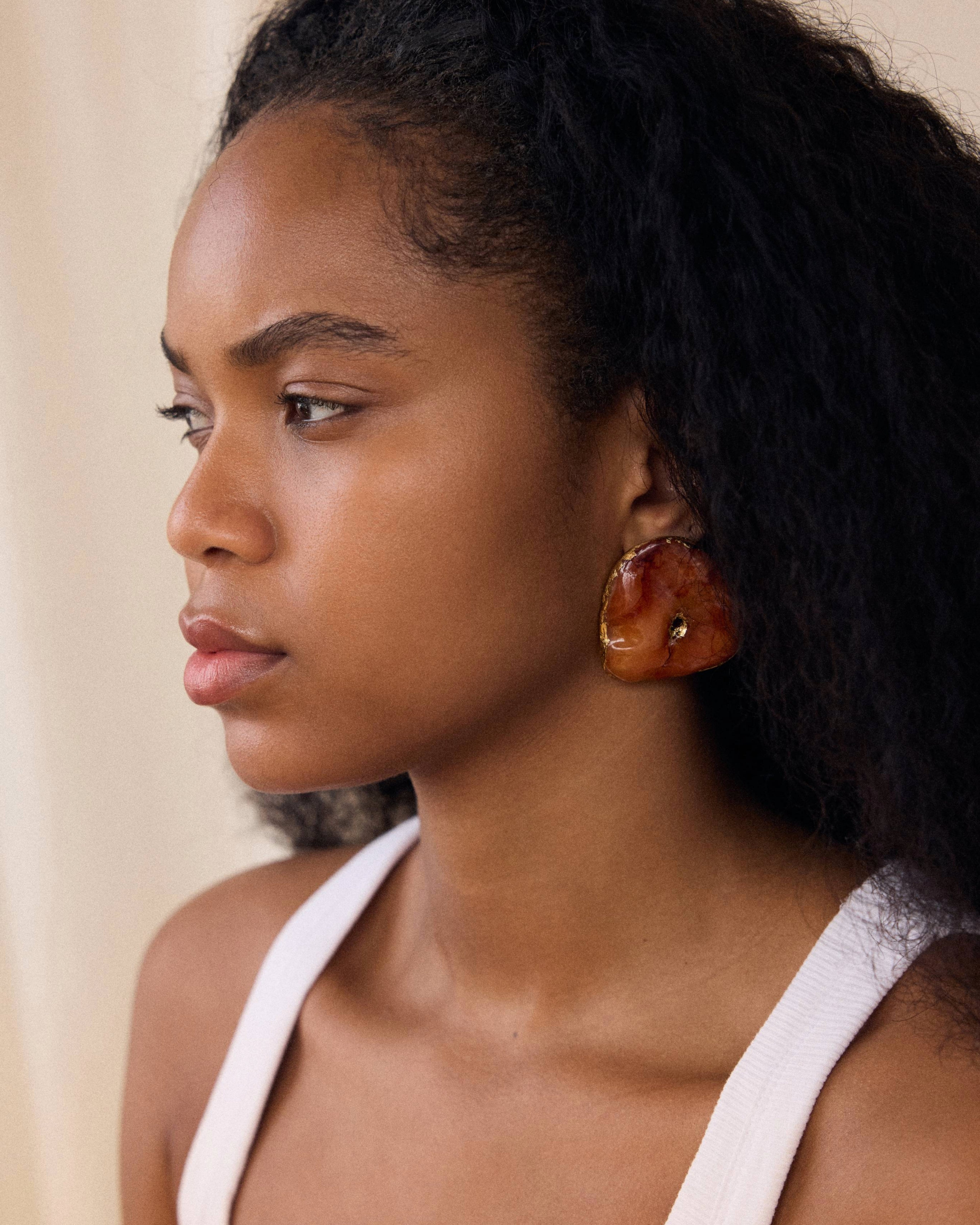 Woman wearing large, round earrings with a neutral background