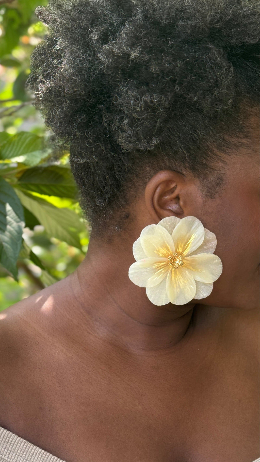 Person wearing a large white flower earring with a natural background