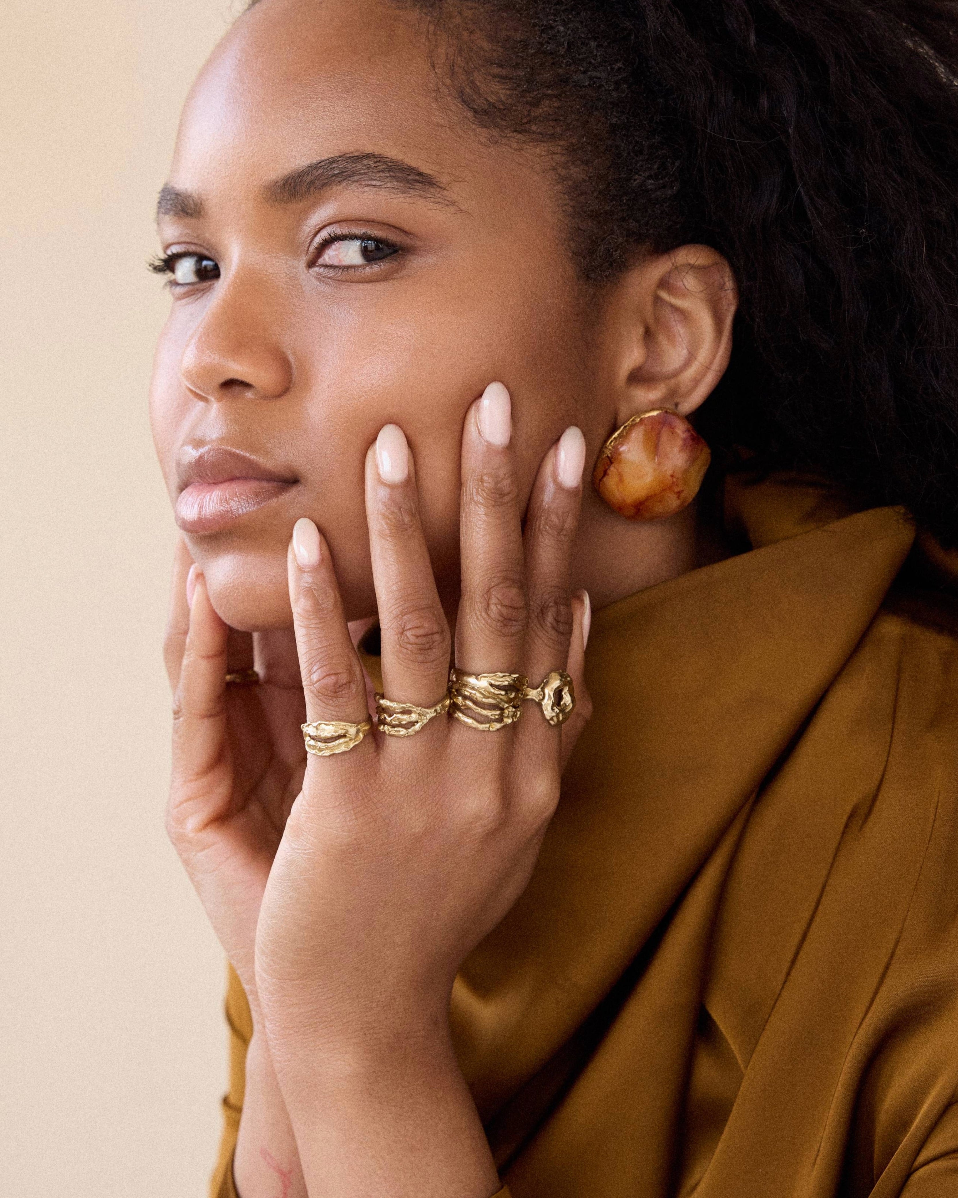 Woman wearing gold jewelry against a beige background