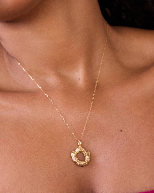 Gold necklace with a circular pendant on a person's neck