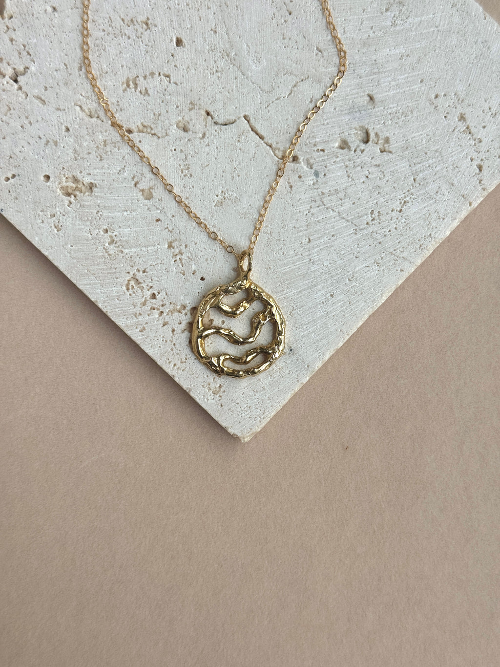 Gold necklace with a circular pendant on a textured stone surface
