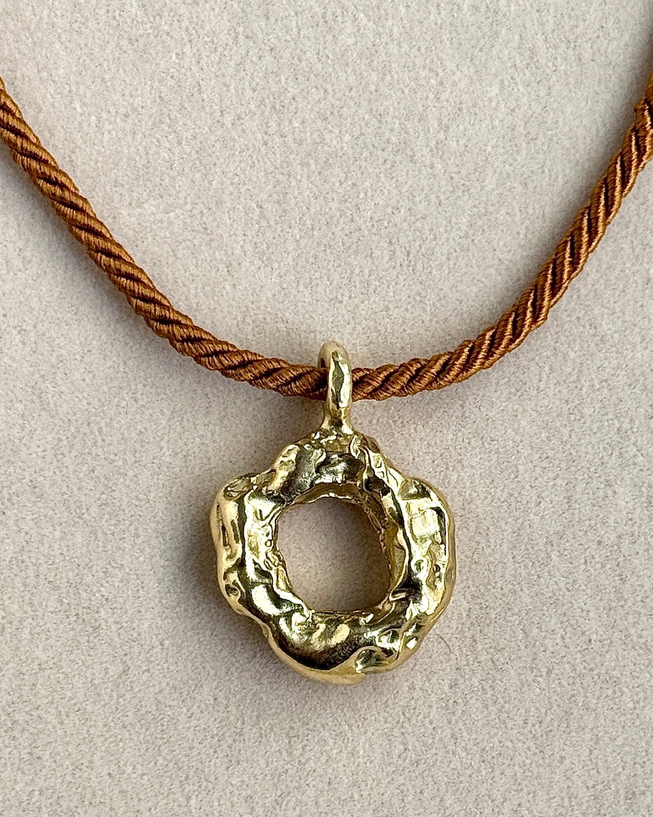 Gold pendant on a brown cord against a beige background