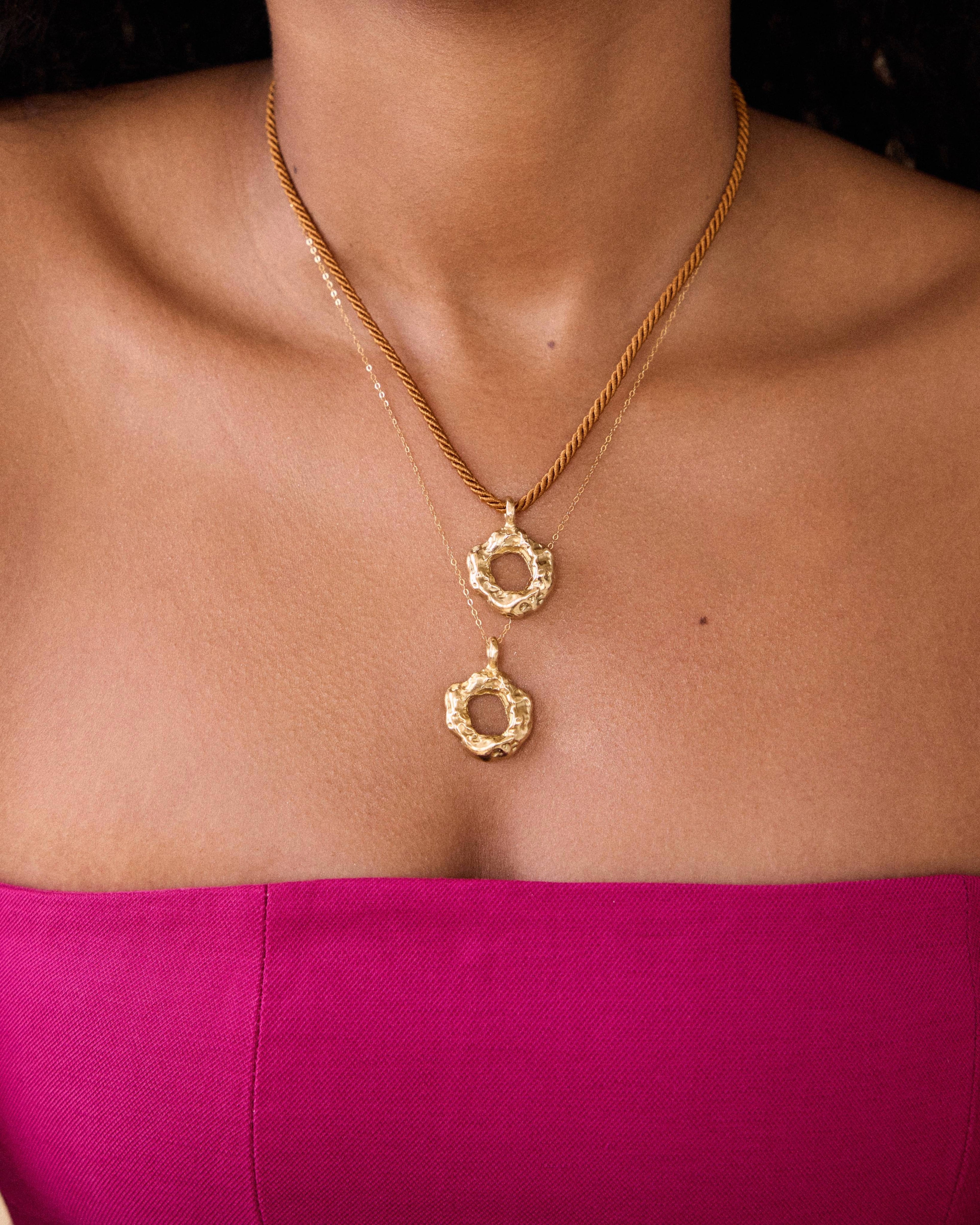 Gold necklace with a pendant on a person wearing a pink top.