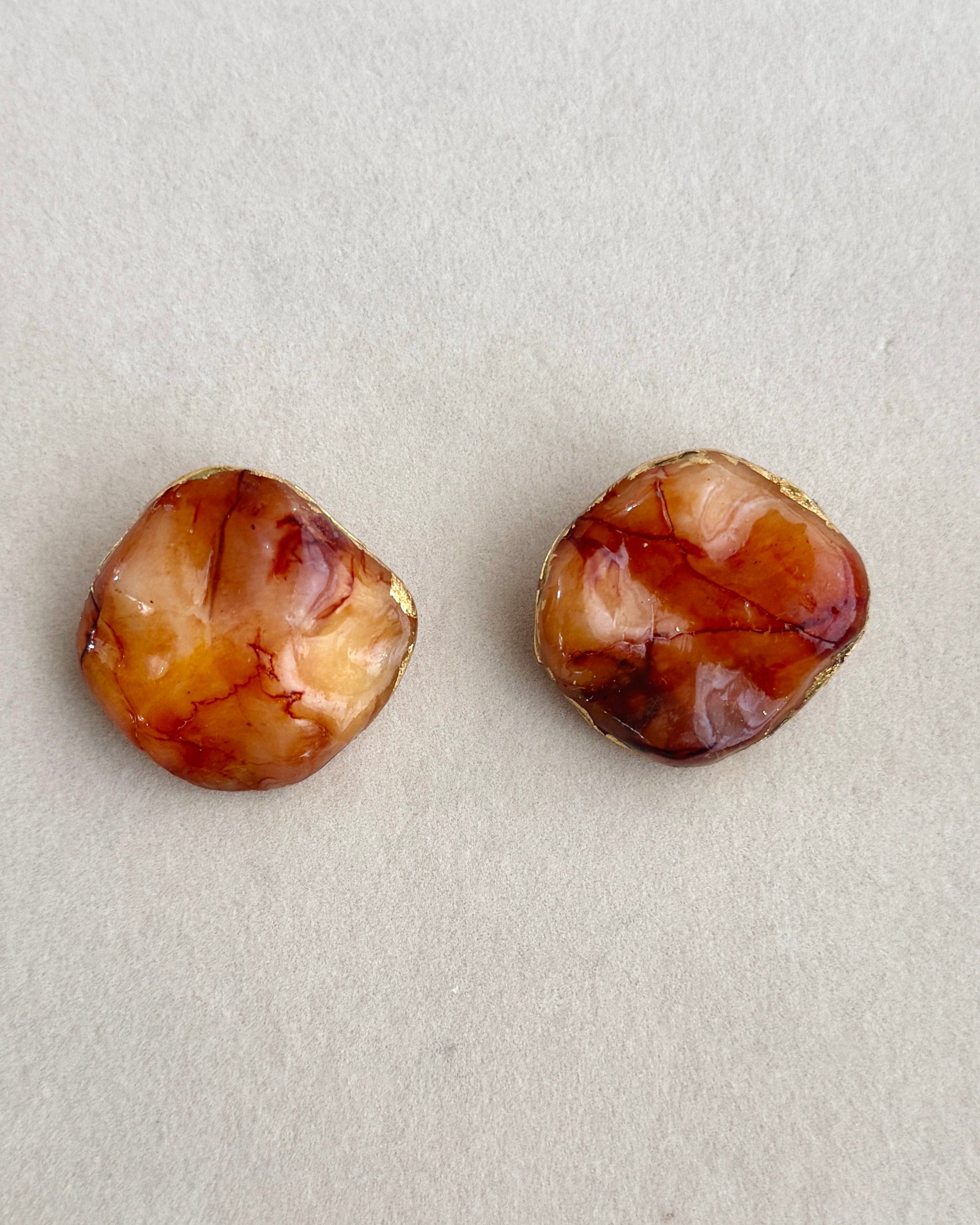 Two round amber stone earrings on a light gray background