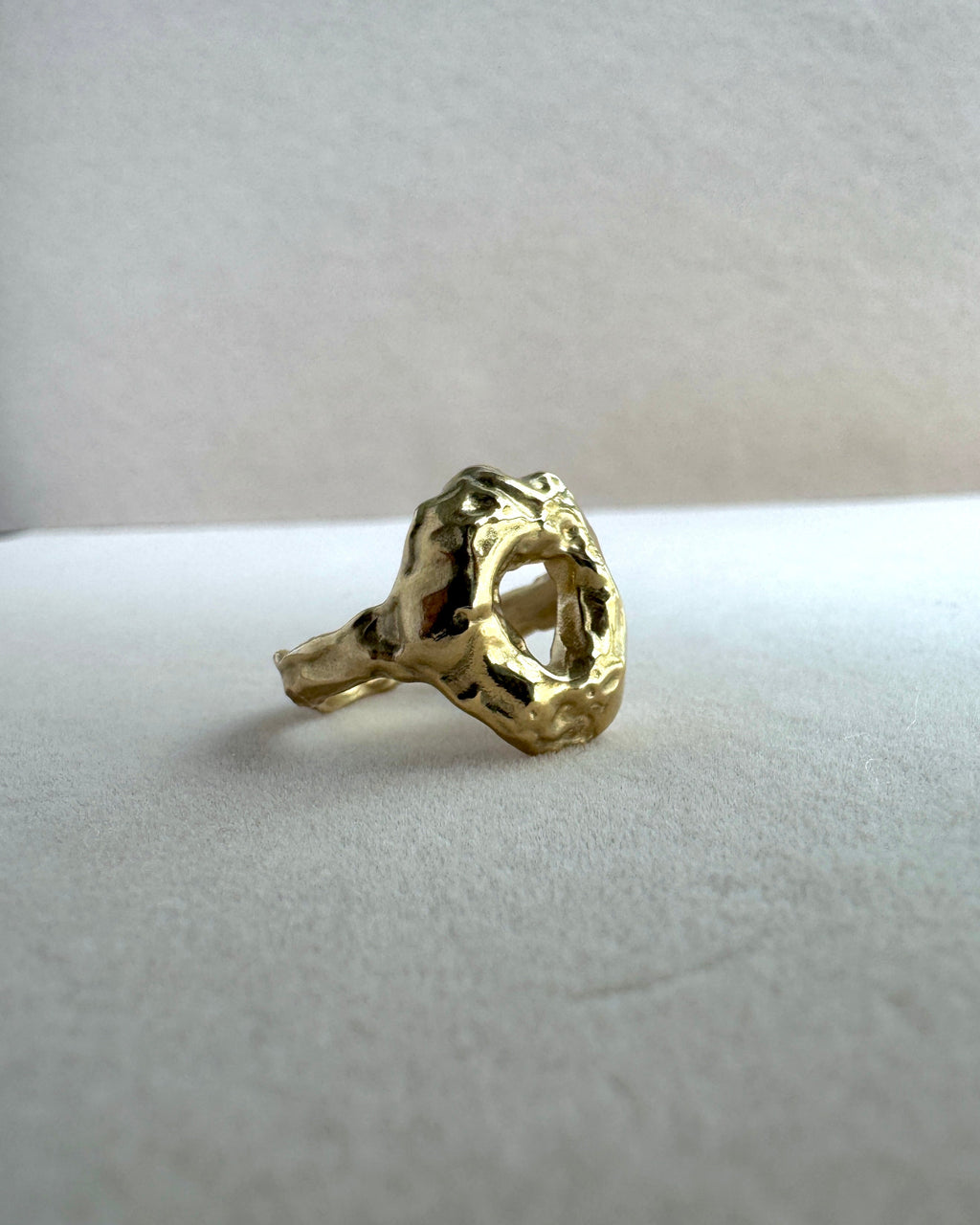 Gold ring with a textured design on a white cushion