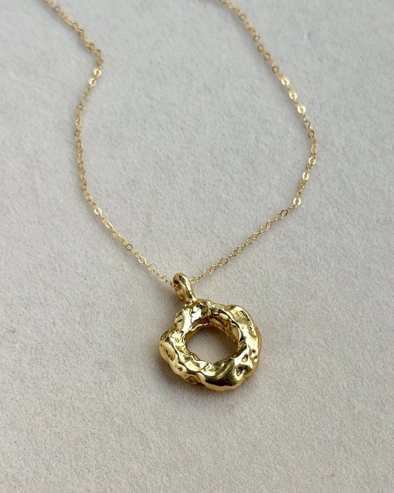 Gold necklace with a textured pendant on a light gray background