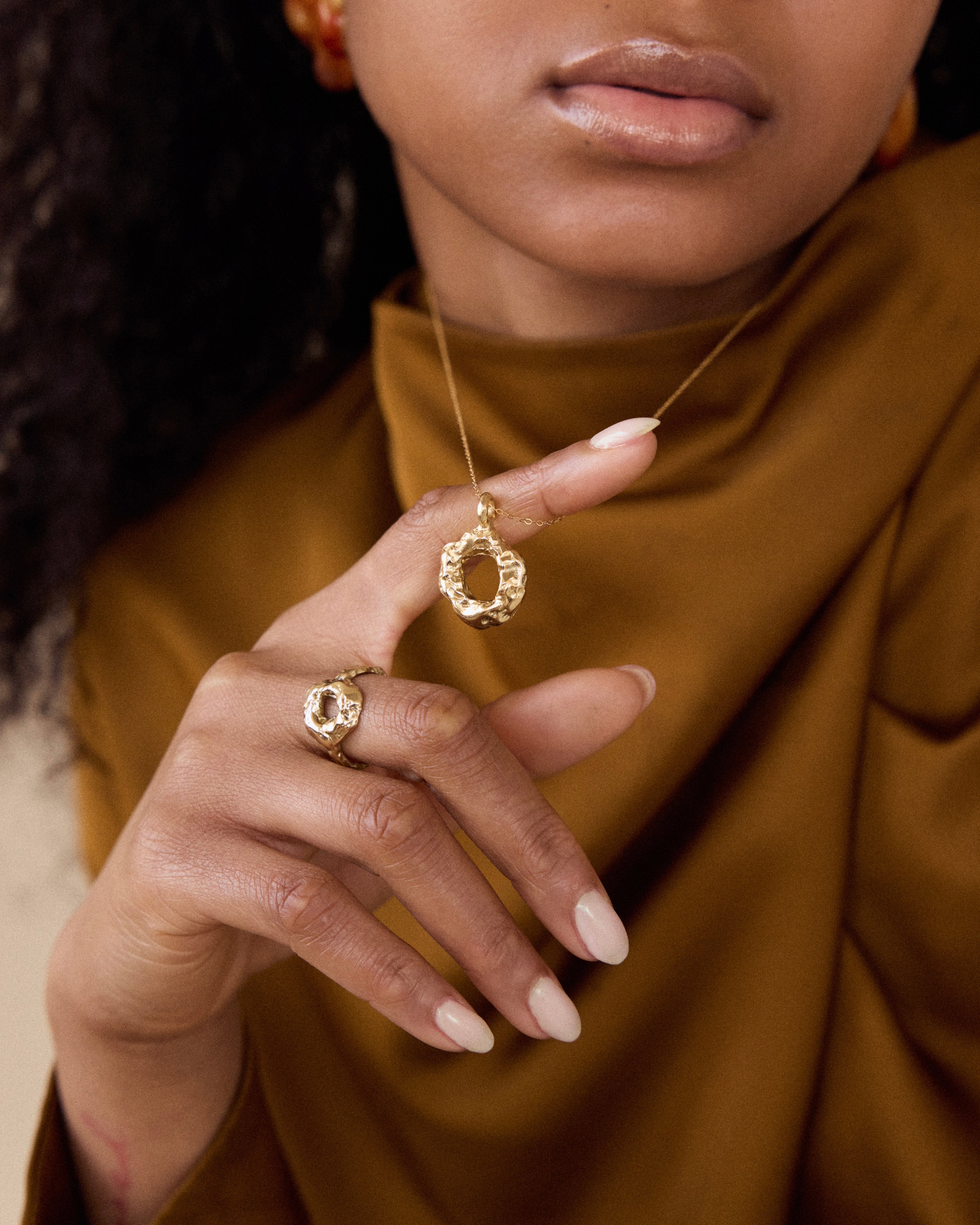 Close-up of a person wearing gold jewelry including a necklace, ring, and earrings.
