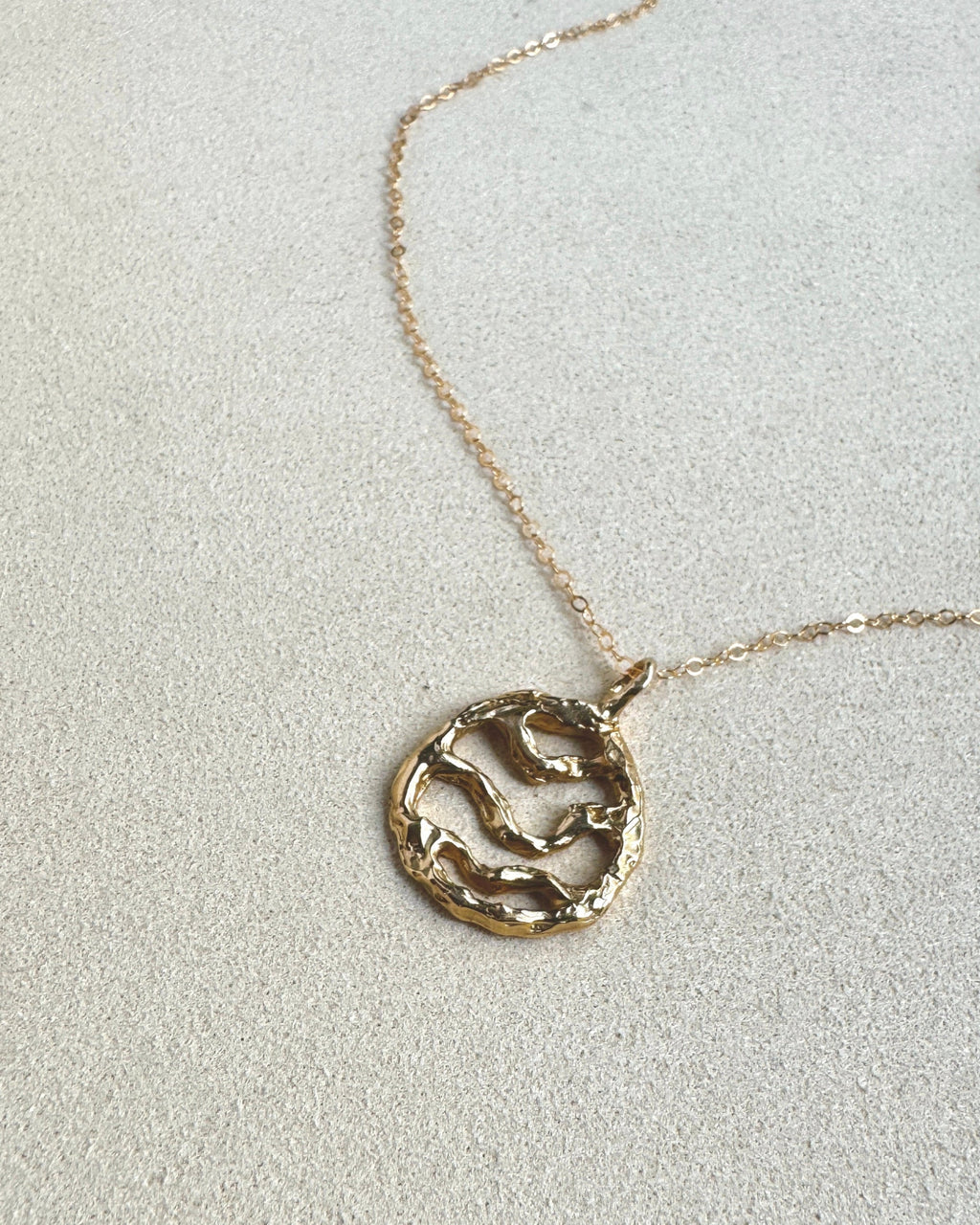 Gold necklace with a circular pendant on a light gray background