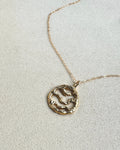Gold necklace with a circular pendant on a light gray background
